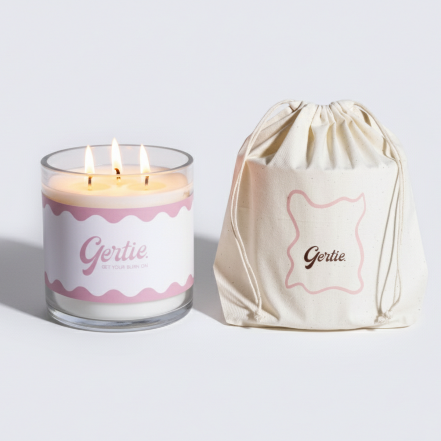 Lit gertie candle with pink label and a matching drawstring bag on a light gray background