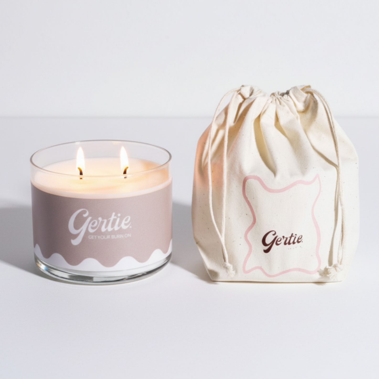 Lit gertie candle with beige label and a matching drawstring bag on a light gray background