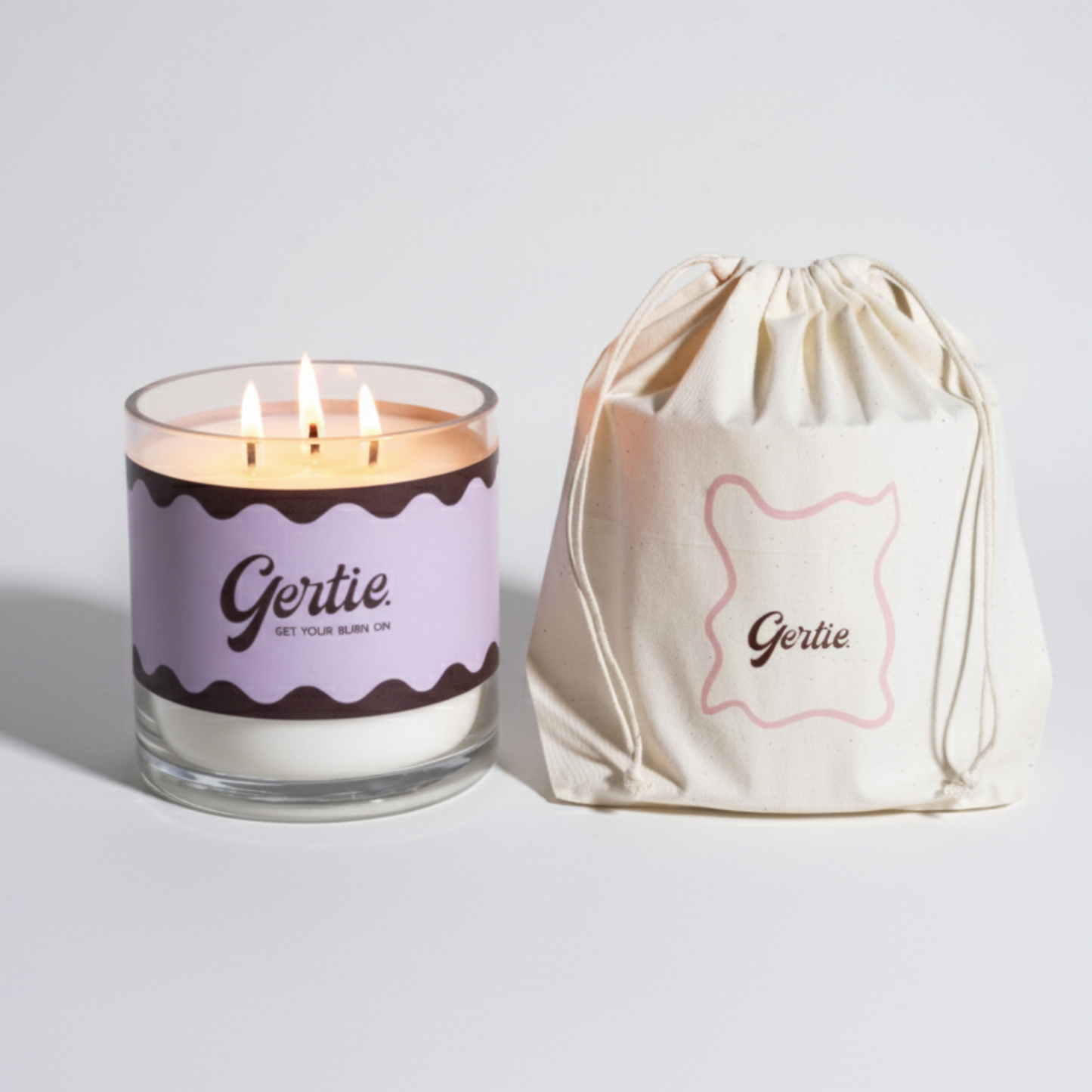 Lit gertie candle with violet label and a matching drawstring bag on a light gray background