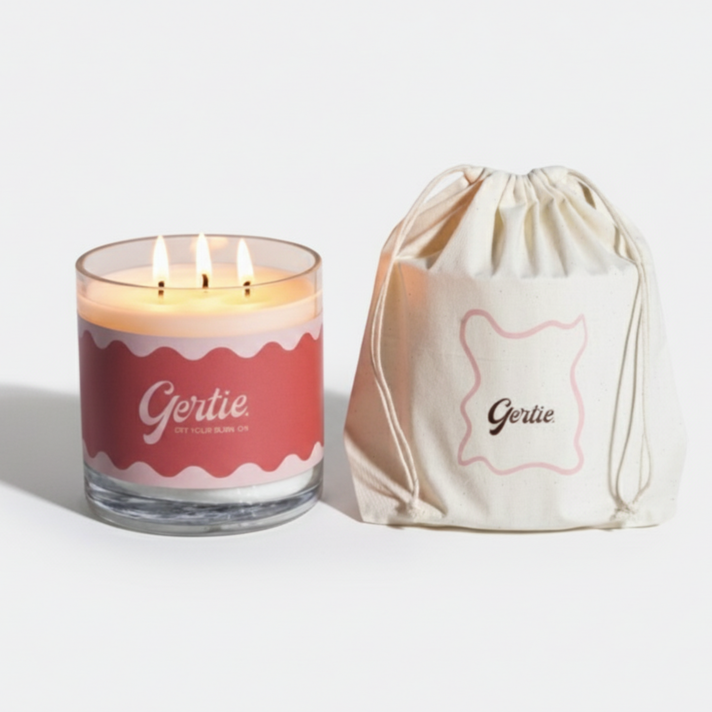 Lit gertie candle with red label and a matching drawstring bag on a light gray background