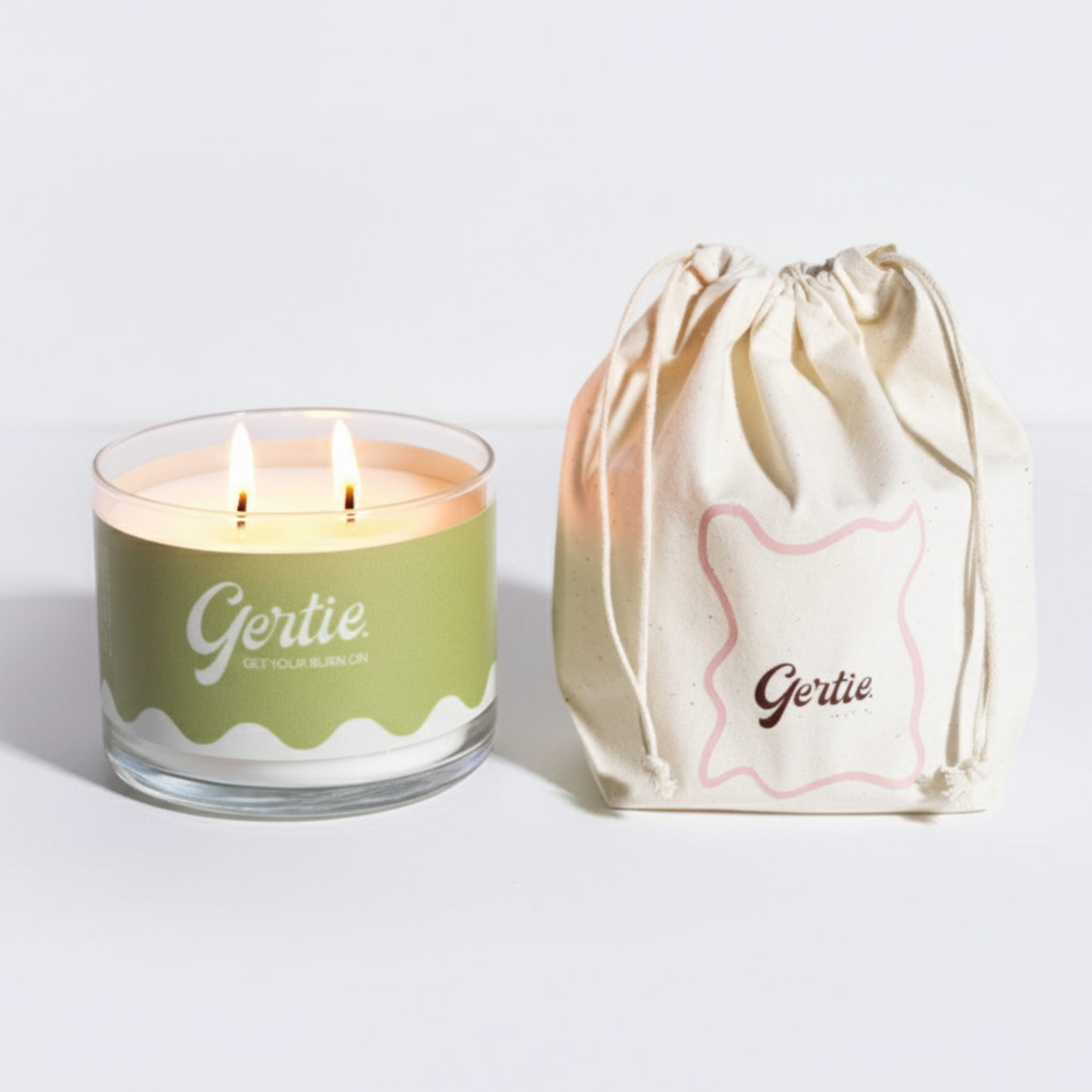 Lit gertie candle with a green label and a matching drawstring bag on a light gray
background