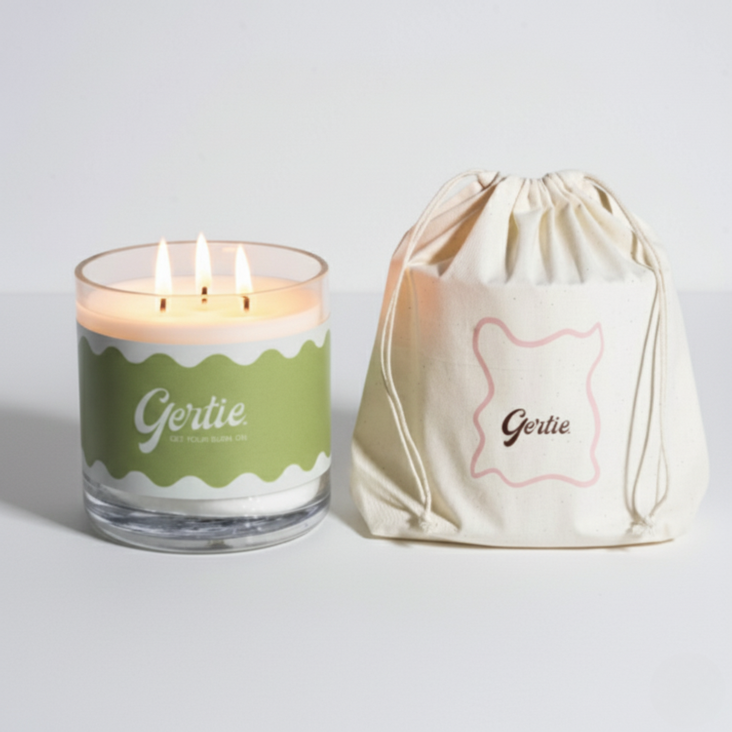 Lit gertie candle with green label and a matching drawstring bag on a light gray background