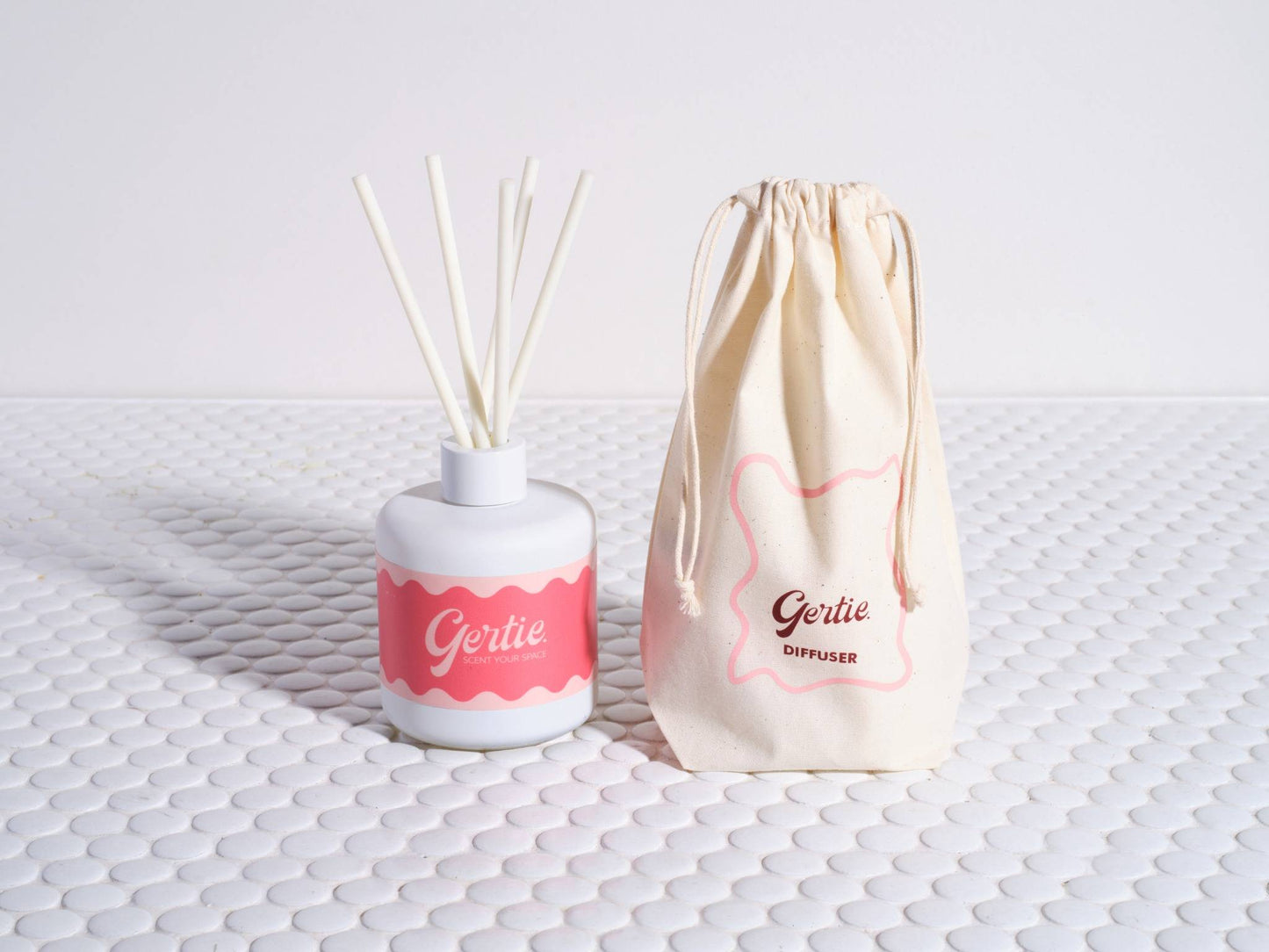 A Pomelo Citrus reed diffuser with a white container and pink label, alongside a reusable cotton pouch with the brand name 'Gertie' printed on it.