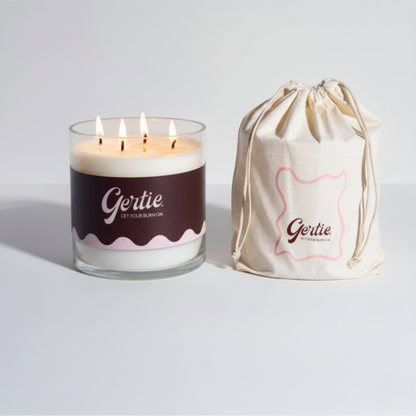 Lit gertie candle with brown label and a matching drawstring bag on a light gray background