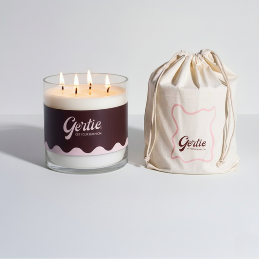 Lit gertie candle with brown label and a matching drawstring bag on a light gray background