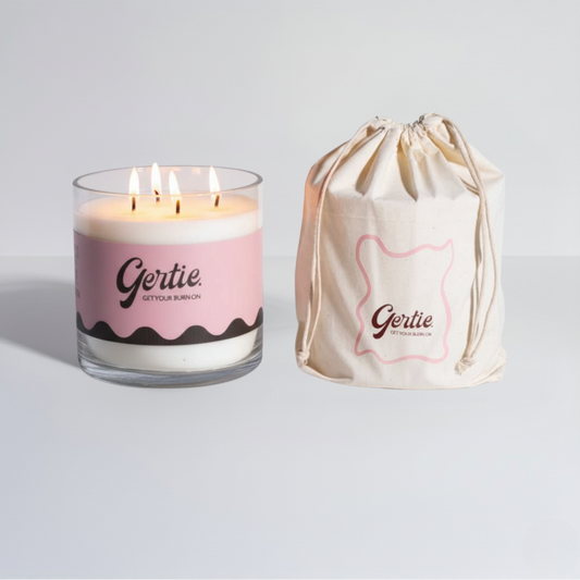Lit gertie candle with pink label and a matching drawstring bag on a light gray background