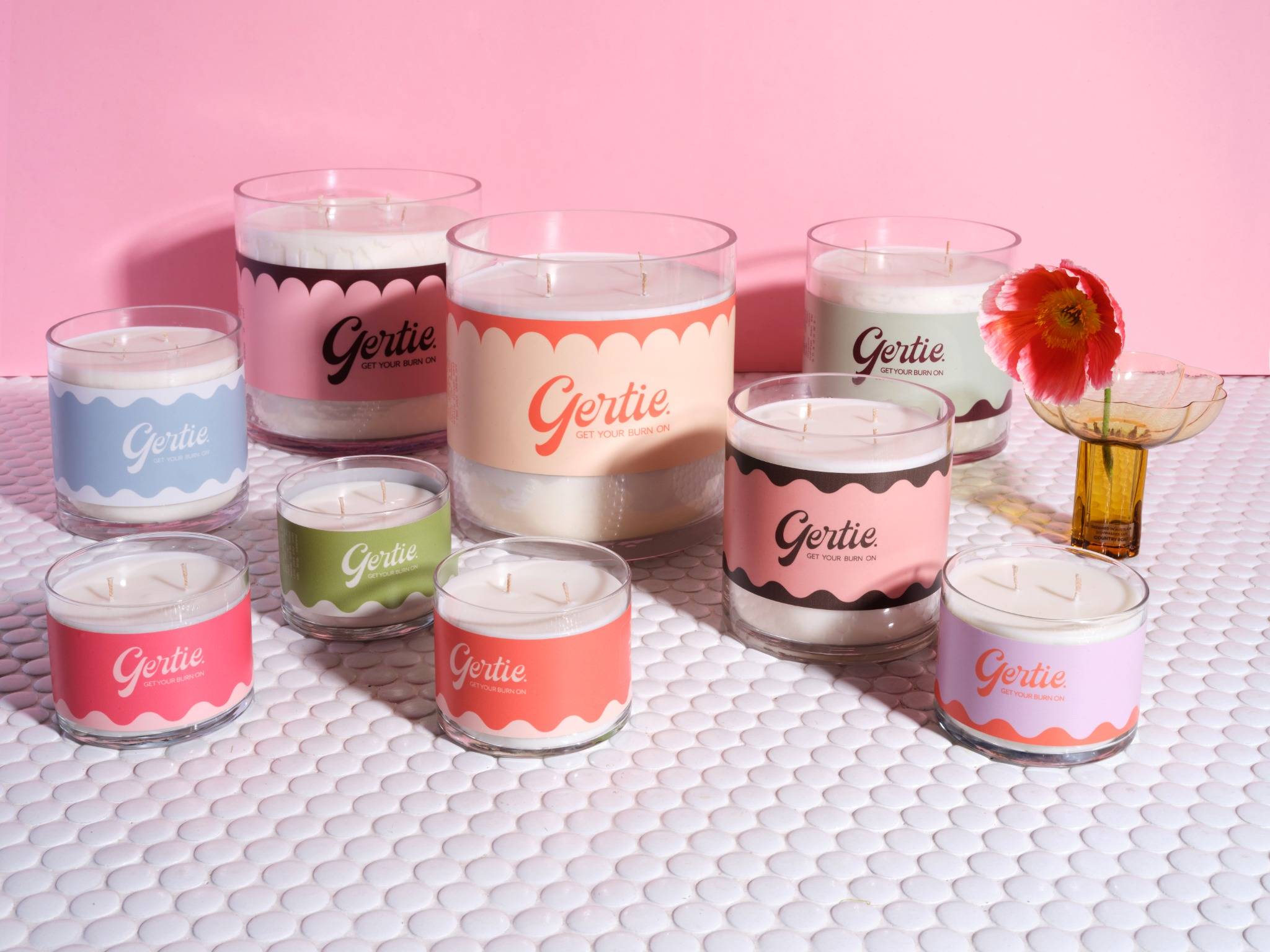 Gertie oversized and standard candles in pastel scalloped labels, styled on white tile with a pink background.