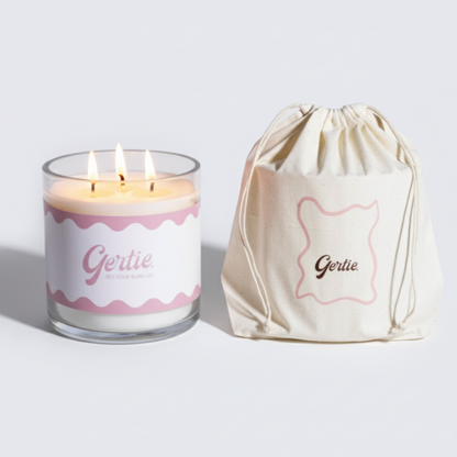 Lit gertie candle with pink label and a matching drawstring bag on a light gray background