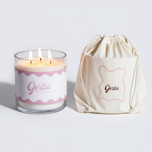 Lit gertie candle with pink label and a matching drawstring bag on a light gray background