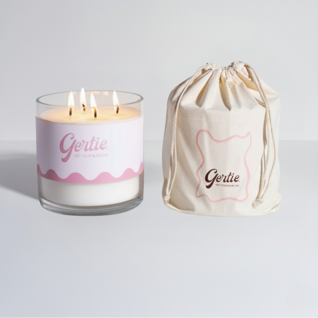 Lit gertie candle with pink and white label and a matching drawstring bag on a light gray background