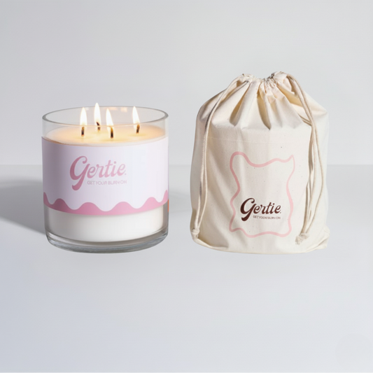 Lit gertie candle with pink and white label and a matching drawstring bag on a light gray background