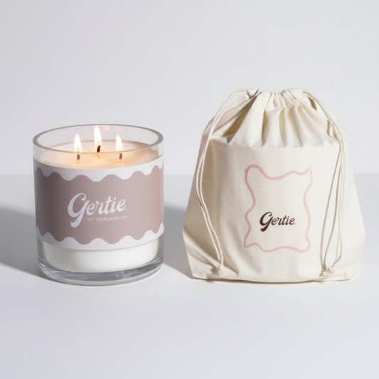 Lit gertie candle with beige label and a matching drawstring bag on a light gray background