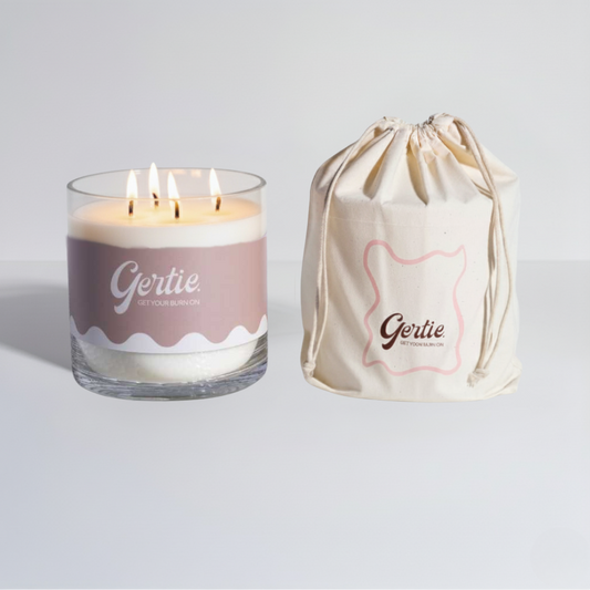 Lit gertie candle with beige label and a matching drawstring bag on a light gray background