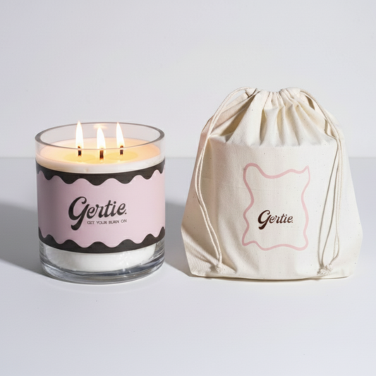 Lit gertie candle with pink label and a matching drawstring bag on a light gray background
