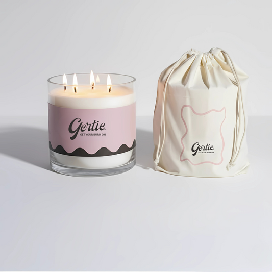 Lit gertie candle with pink label and a matching drawstring bag on a light gray background