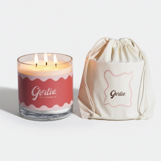 Lit gertie candle with red label and a matching drawstring bag on a light gray background