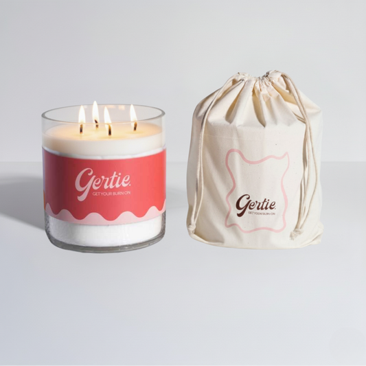 Lit gertie candle with red label and a matching drawstring bag on a light gray background