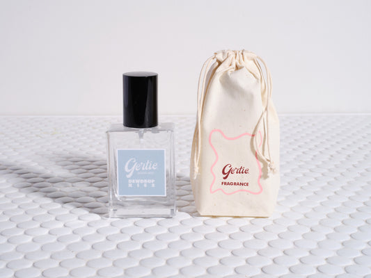 A bottle of Dewdrop Kiss Room Mist with a reusable cotton pouch, both featuring a similar design.