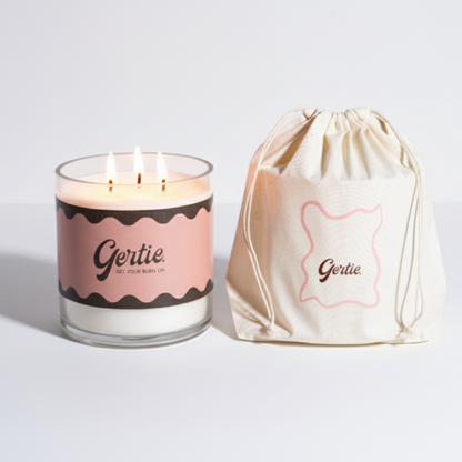 Lit gertie candle with pink label and a matching drawstring bag on a light gray background