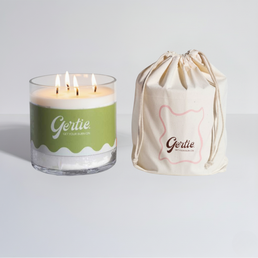 Lit gertie candle with green label and a matching drawstring bag on a light gray background