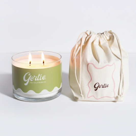  Lit gertie candle with a green label and a matching drawstring bag on a light gray
background