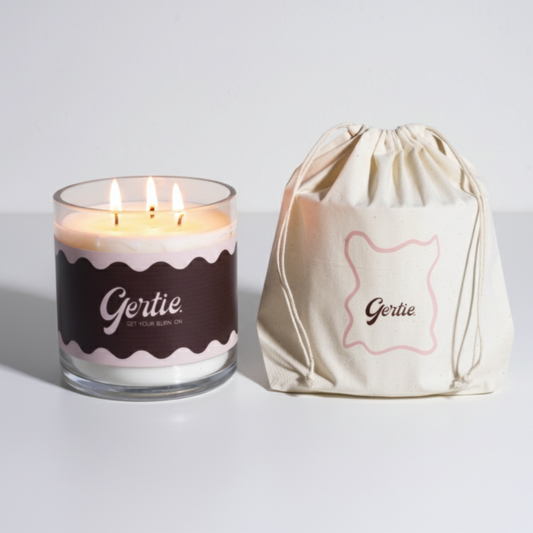 Lit gertie candle with brown label and a matching drawstring bag on a light gray background