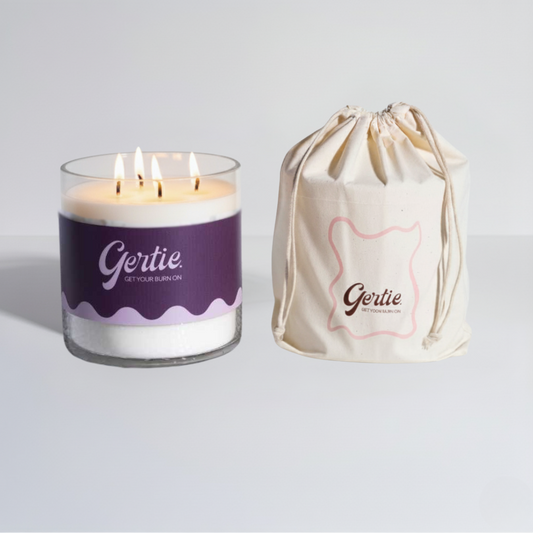 Lit gertie candle with violet label and a matching drawstring bag on a light gray background