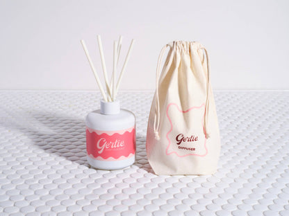 A Pomelo Citrus reed diffuser with a white container and pink label, alongside a reusable cotton pouch with the brand name 'Gertie' printed on it.