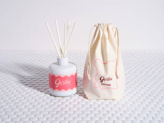 A Pomelo Citrus reed diffuser with a white container and pink label, alongside a reusable cotton pouch with the brand name 'Gertie' printed on it.