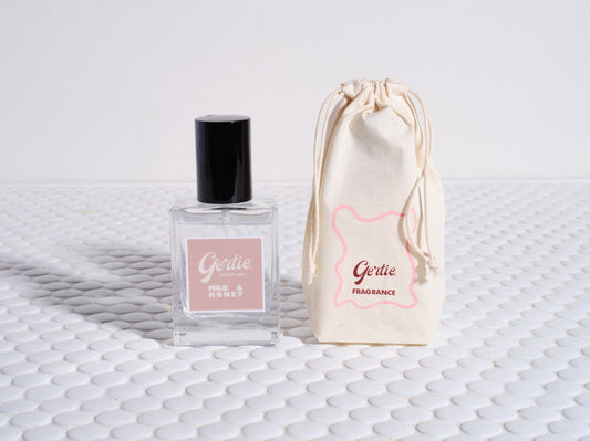 A bottle of 'Milk & Honey Room Mist' with a white label, next to a reusable cotton pouch both with the brand name 'Gertie' on them, presented on a textured white surface.