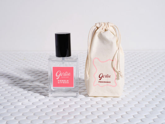 A bottle of 'Pomelo Citrus Room Mist' with a pink label, next to a reusable cotton pouch featuring the product name.